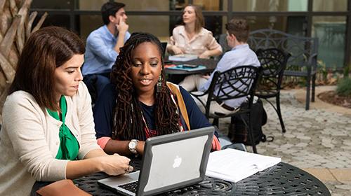 Two students looking at laptop on outdoor table